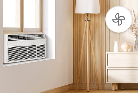 Aire acondicionado de ventana LG en modo ventilador, funcionando en una habitación de tonos cálidos con una lámpara y una cómoda.