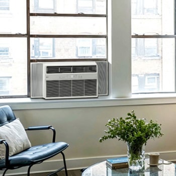 Window air conditioner installed in a living room with a sofa and plants