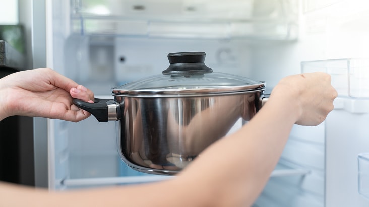 Persona colocando una olla caliente dentro de un refrigerador, que muestra cómo los alimentos calientes pueden elevar la temperatura interna y afectar el rendimiento de refrigeración.
