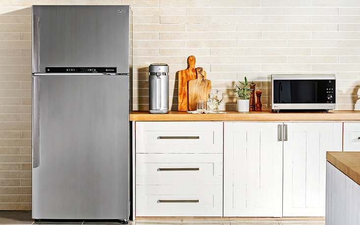 Refrigerador LG con congelador superior colocado en una cocina compacta junto a un microondas pequeño, lo que muestra soluciones prácticas de distribución para espacios reducidos.