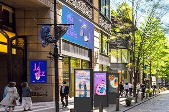 Esta imagen destaca la señalización digital en un espacio exterior, donde se muestran diversos anuncios sobre temas como música, viajes y belleza.