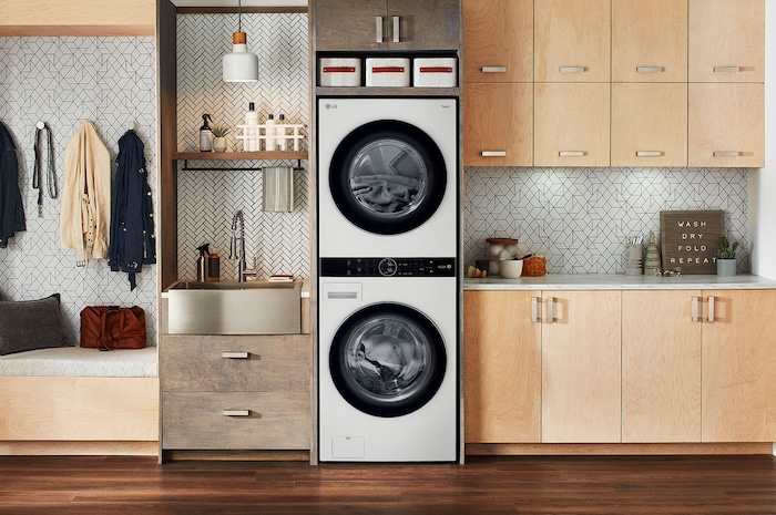 La LG WashTower® WK22WS6E en color blanco (Lavadora 22 kg, Secadora 22 kg), instalada en un moderno cuarto de lavado con gabinetes de madera.