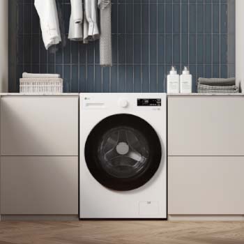 Lavadora de Carga Frontal LG WM16EWNTS6P Blanco Esencia, integrada en un moderno cuarto de lavado con gabinetes beige, fondo de azulejos azules y suelo de madera.