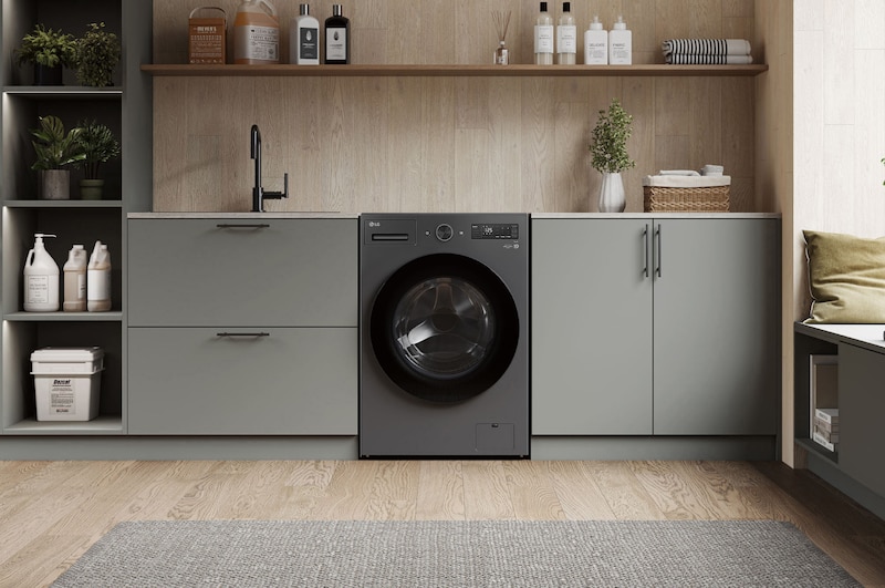 Lavadora de Carga Frontal LG WD20EGNTS6P Grafito Esencia, integrada en un moderno cuarto de lavado con gabinetes gris-beige y encimeras de madera.