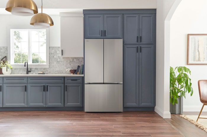 Refrigerador French Door LG GM90BIP Prime Silver, integrado en una cocina moderna con gabinetes azul marino, paredes blancas y lámparas colgantes doradas.