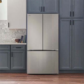 Refrigerador French Door LG GM90BIP Prime Silver, integrado en una cocina moderna con gabinetes azul marino, paredes blancas y lámparas colgantes doradas.