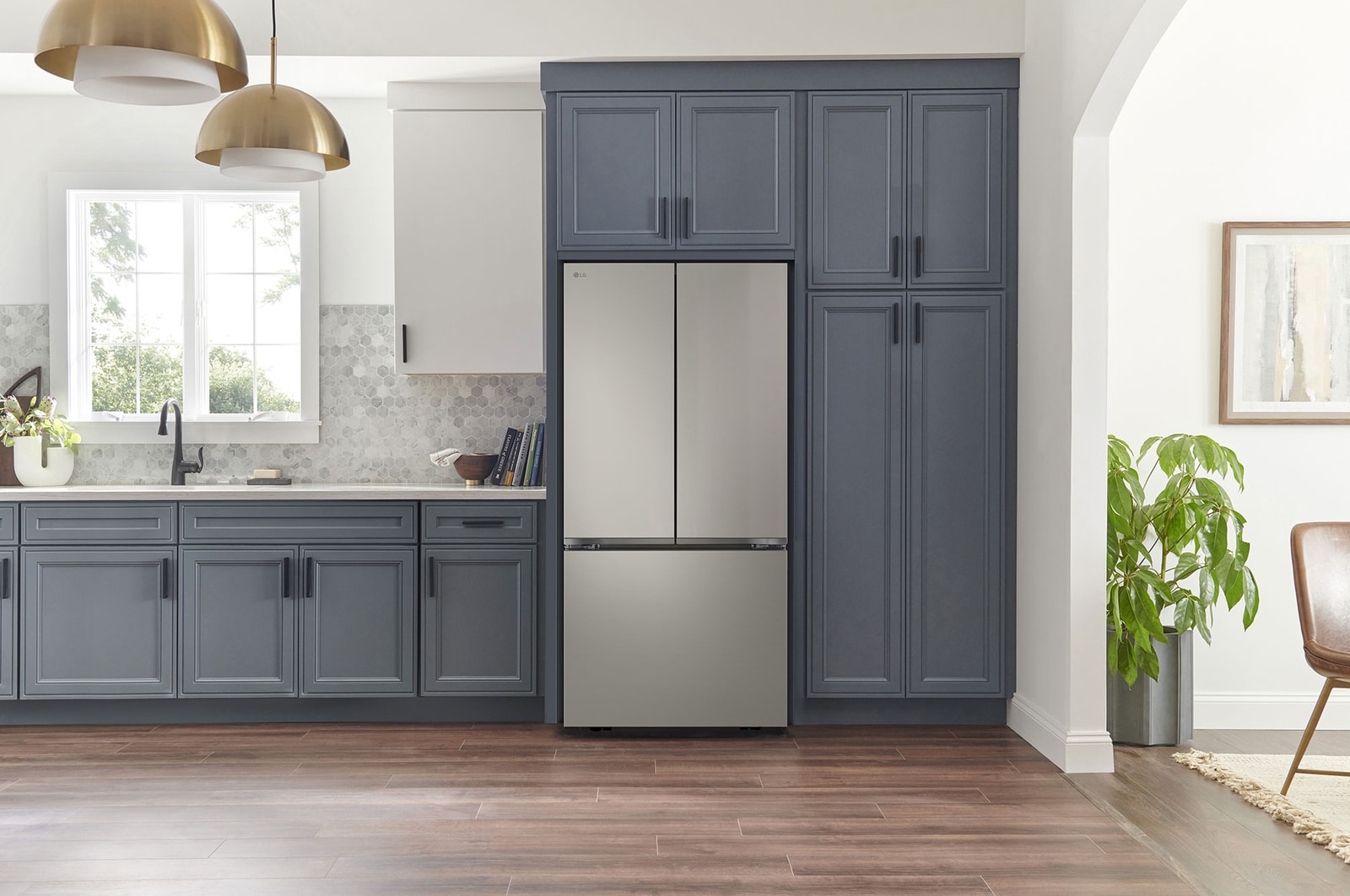 Refrigerador French Door LG GM65BPP Prime Silver, integrado en una cocina moderna con gabinetes azul marino, paredes blancas y lámparas colgantes doradas.