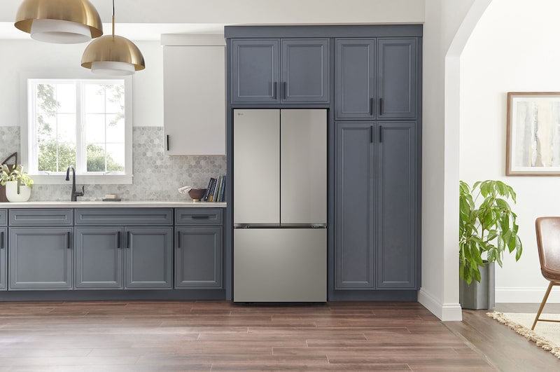 Refrigerador French Door LG GM65BPP Prime Silver, integrado en una cocina moderna con gabinetes azul marino, paredes blancas y lámparas colgantes doradas.