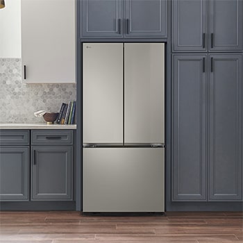 Refrigerador French Door LG GM65BPP Prime Silver, integrado en una cocina moderna con gabinetes azul marino, paredes blancas y lámparas colgantes doradas.