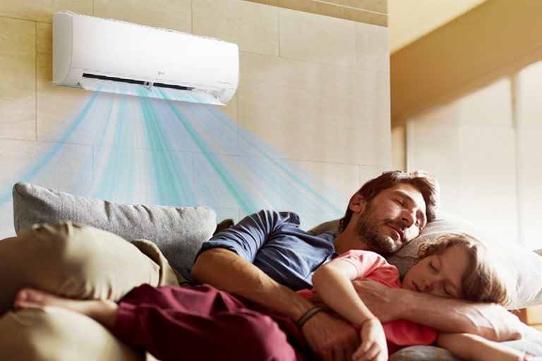 Un padre y su hija durmiendo en el sofá bajo el aire acondicionado que sopla aire sobre ellos.