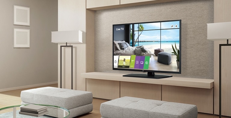 A TV sits on the wall shelf of a large hotel room with a sea view.