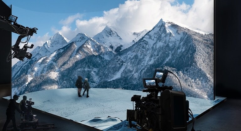 Un estudio de producción virtual con paredes LED curvas y LED en el techo y el piso está filmando un video de un paisaje de montaña nevada.