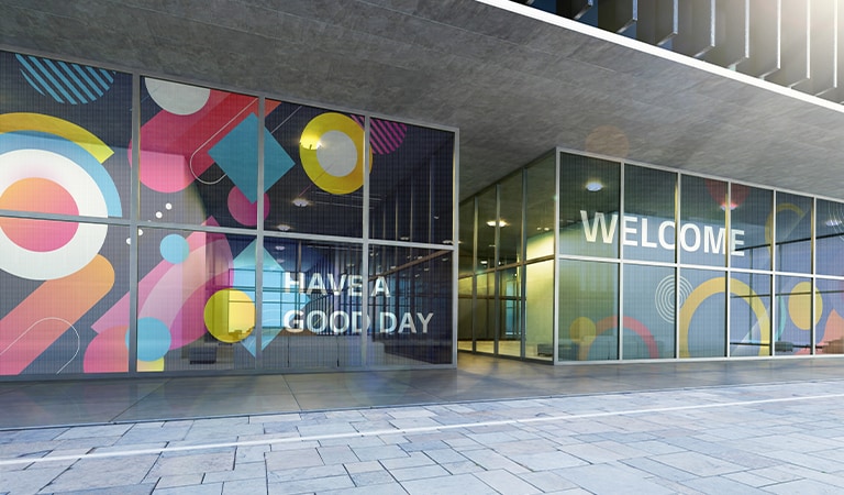 Las películas LED transparentes instaladas en la pared de vidrio en la entrada del edificio muestran contenido de bienvenida a los visitantes. Parte del contenido muestra bien el color, y parte parece lo suficientemente transparente como para que se vea el fondo detrás de las películas LED.
