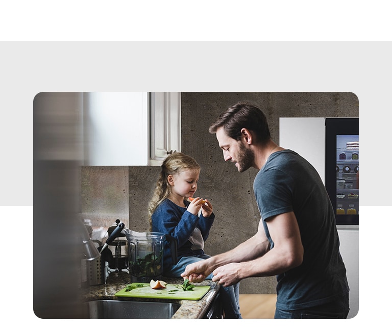A child is sitting in the kitchen sink and a man cooks in front of him