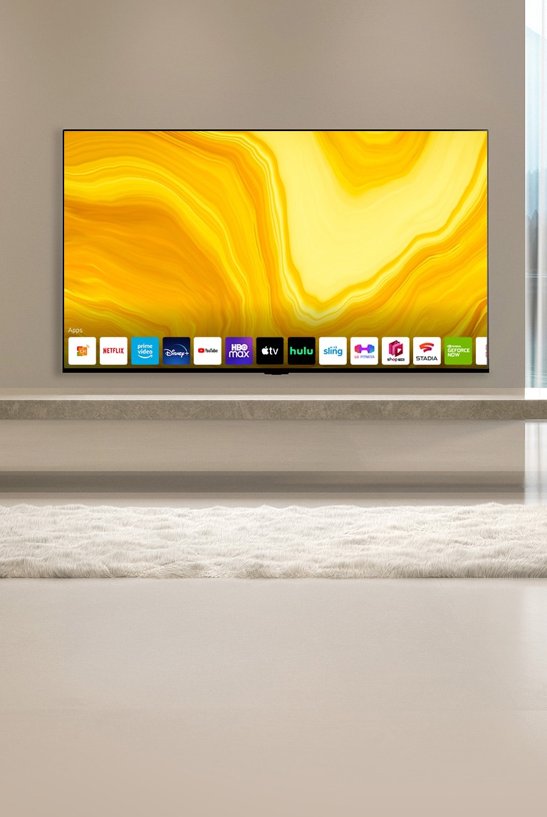 La pantalla de inicio se desplaza hacia abajo y la escena cambia para mostrar un televisor colgado en una sala de estar de apariencia cálida que muestra la pantalla de inicio. 