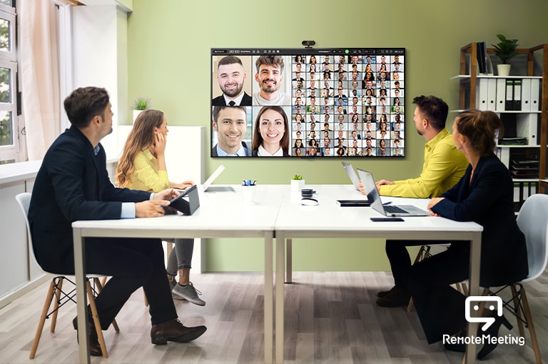 Hay cuatro personas sentadas en la sala de conferencias mirando un televisor y participando de una teleconferencia. La pantalla del televisor muestra los rostros de las personas que participan de la reunión.