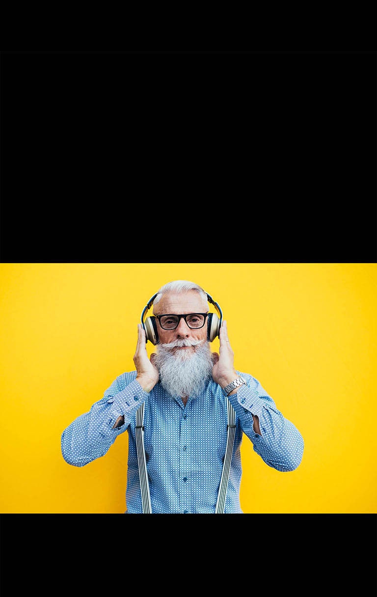 Un abuelo está parado frente a una pared amarilla, con auriculares.