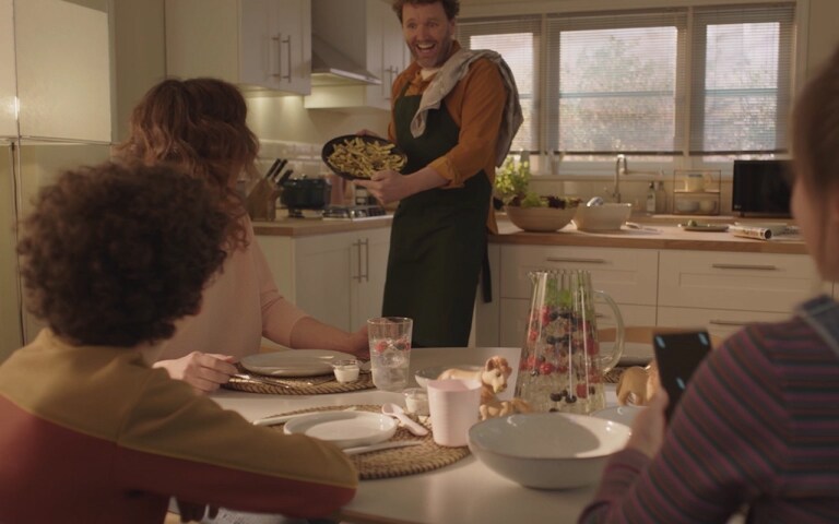 Un hombre le muestra a su familia un plato que acaba de cocinar. Esta imagen cambia para mostrar la otra imagen. Los calabacines fritos se cocinan en el microondas.