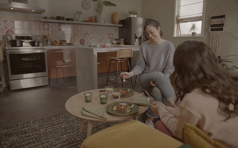 Imagen de dos mujeres comiendo sobre la base de una cocina con una estufa instalada.