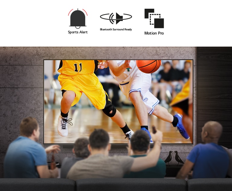 Vista posterior de un grupo de hombres sentados frente a un gran televisor montado en la pared. La pantalla muestra jugadores de baloncesto.