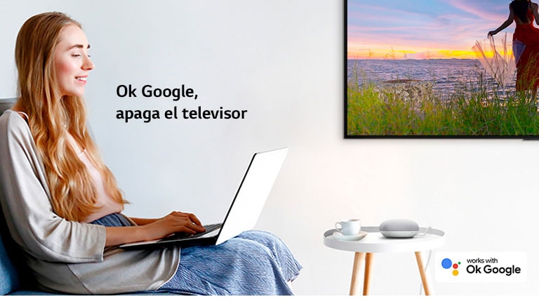 Una mujer sentada en un sofá con un portátil en una habitación con un televisor en la pared ordena a un altavoz de IA que apague el televisor.