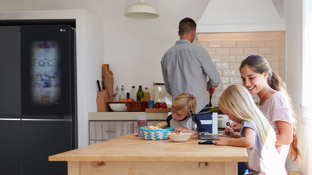 Toda la familia está sentada a la mesa preparando una comida. El refrigerador InstaView instalado en un lado de la cocina está creando aire frío rápidamente.