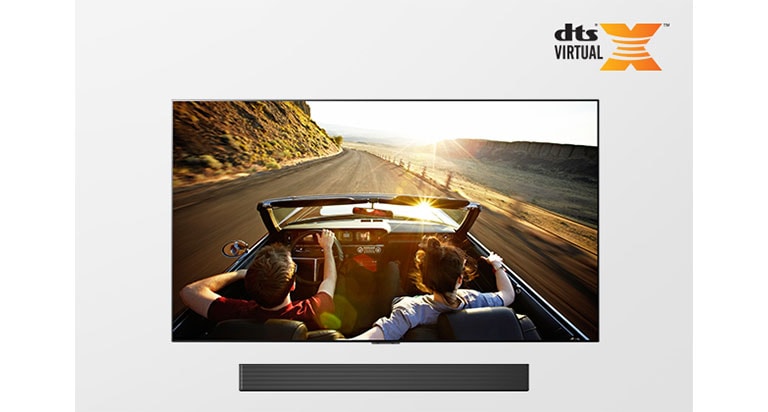 TV y barra de sonido juntos a la vista. La televisión muestra a una pareja en un automóvil de techo abierto en la carretera conduciendo hacia la puesta de sol.