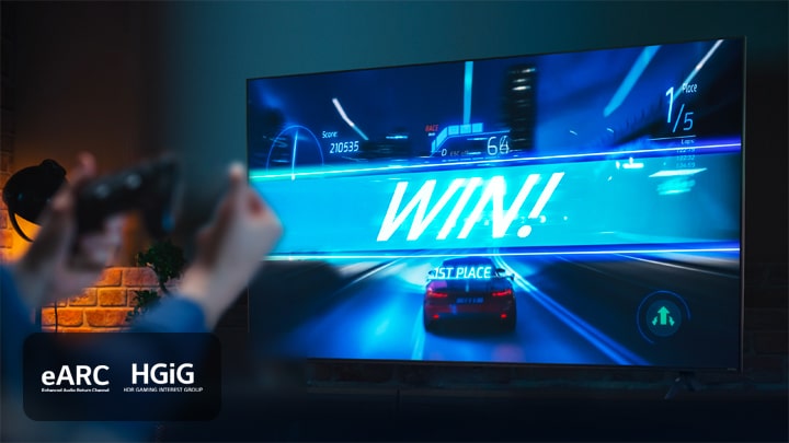 Un juego de carreras de coches en la línea de meta, con el cartel que dice "¡GANA!", mientras el jugador agarra el joystick del juego. Los logotipos de eARC y HGiG se encuentran en la esquina inferior izquierda.