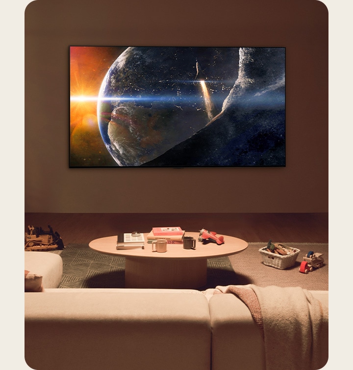 Una familia sentada cerca de una pequeña mesa en el piso de una sala de estar poco iluminada mira hacia arriba a un televisor LG montado sobre la pared, que muestra una imagen de la Tierra vista desde el espacio.