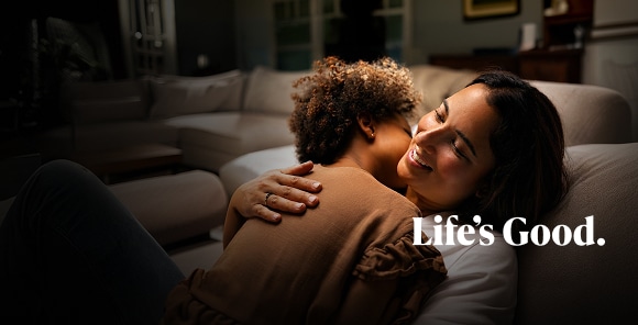 Una mujer sonriendo mientras abraza a un niño pequeño, con el texto pequeño 'Life's Good' debajo.
