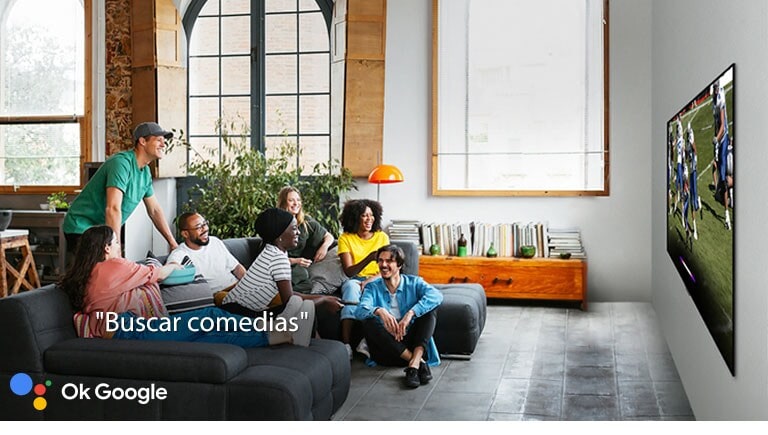 Mujer viendo el fútbol en la televisión con amigos y pidiendo al Asistente de Google que busque comedias.