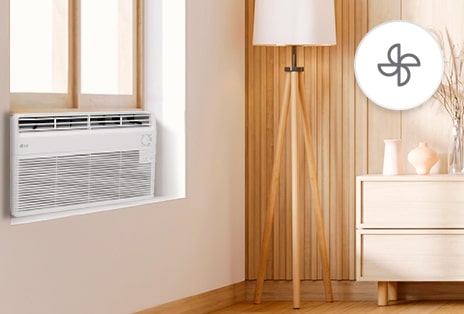 Aire acondicionado de ventana LG en modo ventilador, funcionando en una habitación de tonos cálidos con una lámpara y una cómoda.