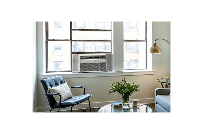 Window air conditioner installed in a living room with a sofa and plants