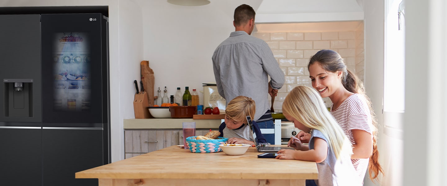 Toda la familia está sentada a la mesa preparando la comida. El refrigerador InstaView instalado en un lado de la cocina está generando aire frío rápidamente.
