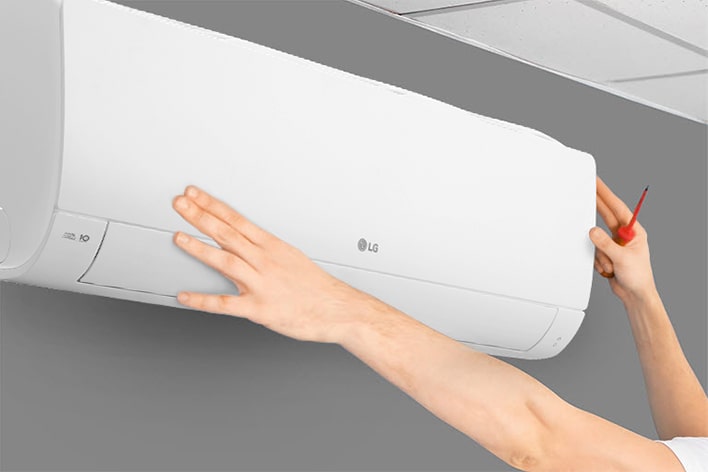 The side view of the air conditioner can be seen. Two hands are reaching up holding a tool, showing the ease of installation.