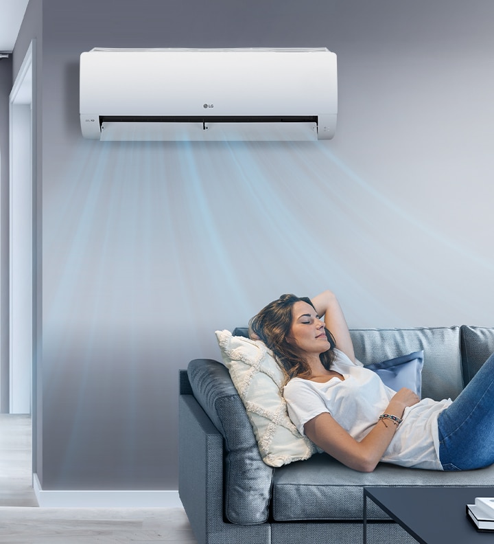 A woman lounges on a couch with the LG AC on the wall above her. Streams of air indicates it is on and cooling the room.