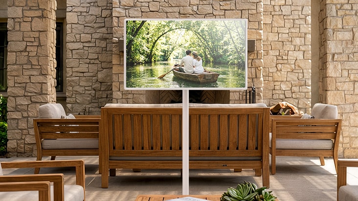 LG StanbyME 2 Max LX6 Movable Screen with a Built-in Battery stands among wooden furniture in a stone-walled courtyard, supporting over four hours of wireless playback for flexible viewing without a power connection.