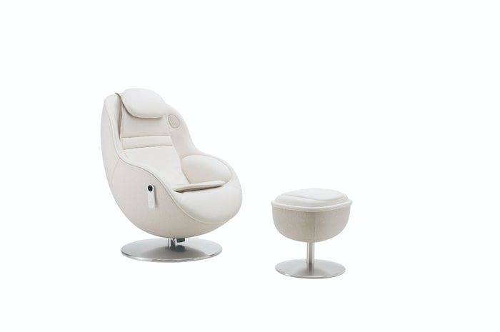 Angled white massage chair and footstool highlighting its curved silhouette on a neutral backdrop.