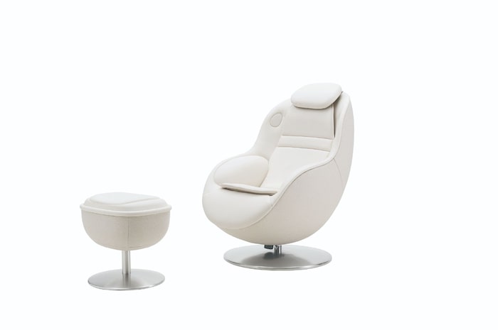 White massage chair with matching round footstool on a metal pedestal against a light background.
