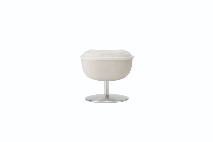 White round footstool on a metal pedestal, serving as the chair’s matching ottoman in a neutral setting.