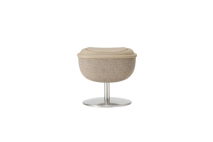 White round footstool on a metal pedestal, serving as the chair’s matching ottoman in a neutral setting.