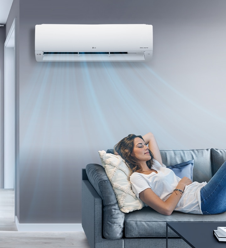 A woman lounges on a couch in a living room with the LG air conditioner installed above her on the wall. Blue streams of air are on the image to indicate it is on and cooling the room.