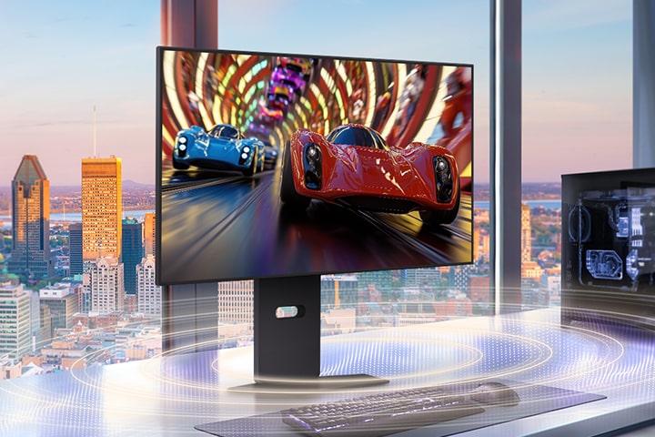 A sleek gaming monitor on a modern desk displays a high-speed racing game with two sports cars, one red and one blue, speeding through a vibrant tunnel. The setup is placed in front of large windows overlooking a city skyline at sunset, with a gaming PC on the right and soundwave graphics illustrating immersive audio effects.	