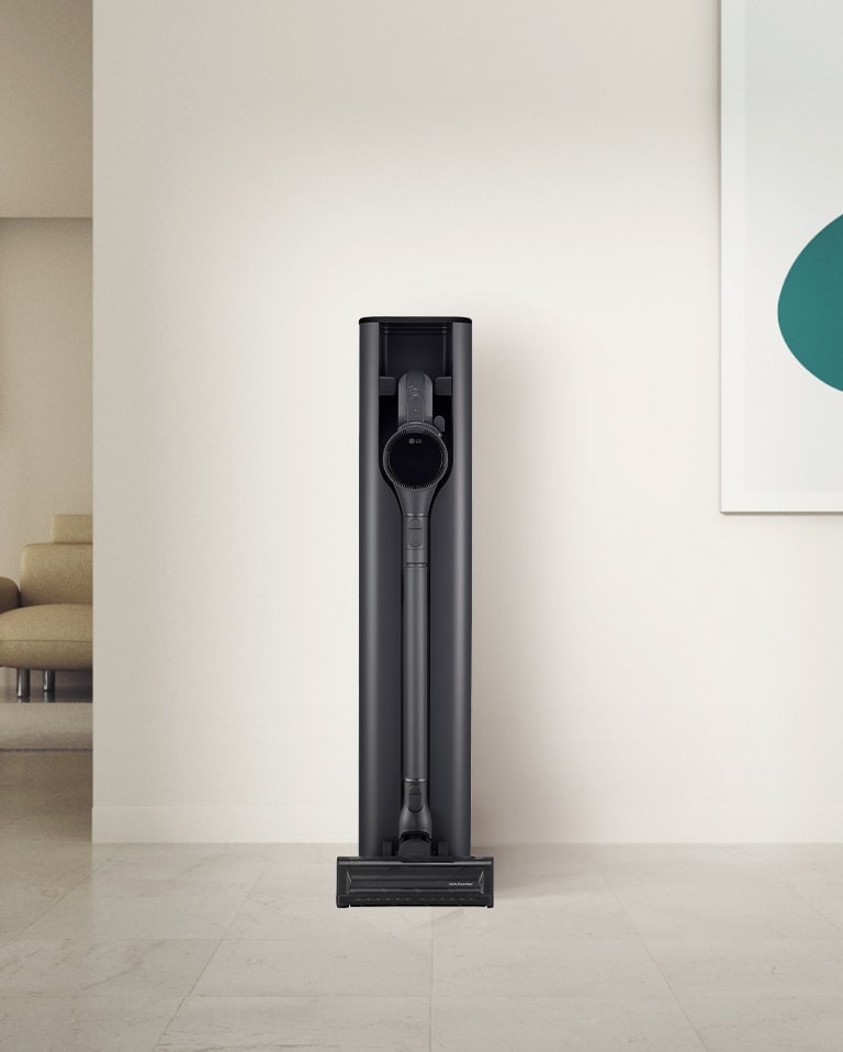 LG cordless vacuum cleaner neatly placed in its charging dock, against a minimalist wall with art and a couch nearby.