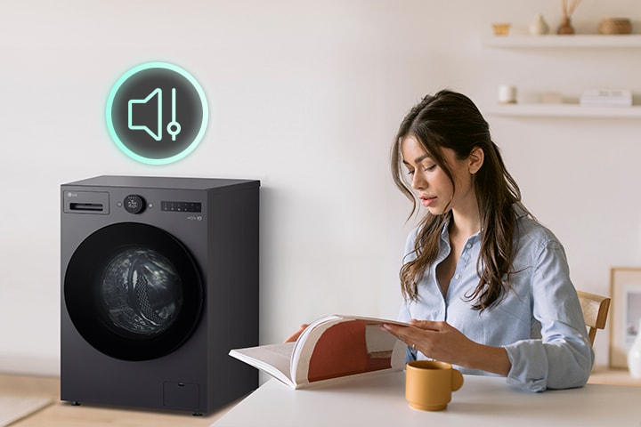 The woman is sitting at a table reading a book and showing icons and washing machines that have less noise next to her