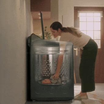 Woman putting clothes in and taking them out of the top load washing machine