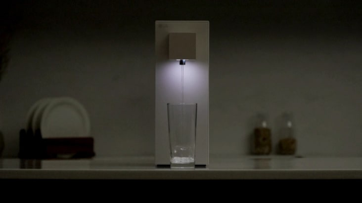 LG water purifier with the dispensing light on in a dark kitchen.