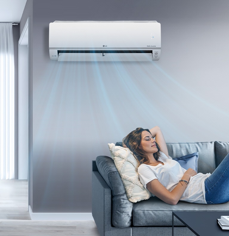 A woman lounges on a couch with the LG AC on the wall above her. Streams of air indicates it is on and cooling the room.