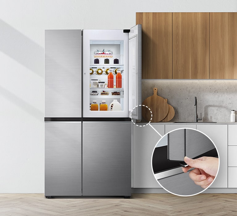 A front view of the refrigerator installed in a kitchen. The top right door is open and there is a circle and a line leading to a larger circle that shows a magnified view of the button on the bottom left corner of the open door which has a concealed opening button.