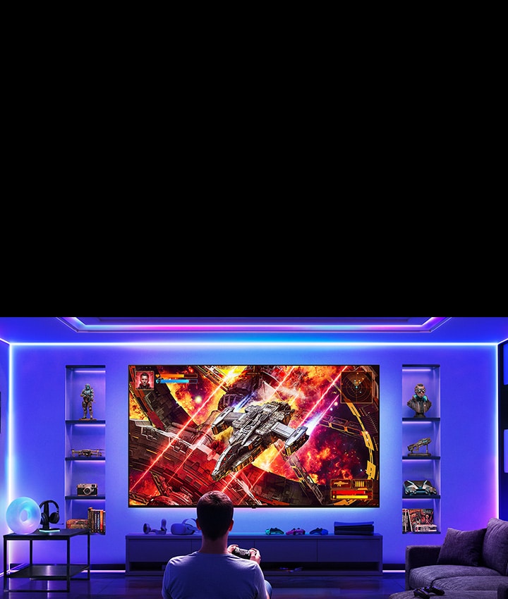 LG TV with clutter-free setup shows a wall-mounted TV in a gaming room, where minimal visible cables create a clean environment as a player faces the screen, illustrating a streamlined and flexible wireless gaming setup.